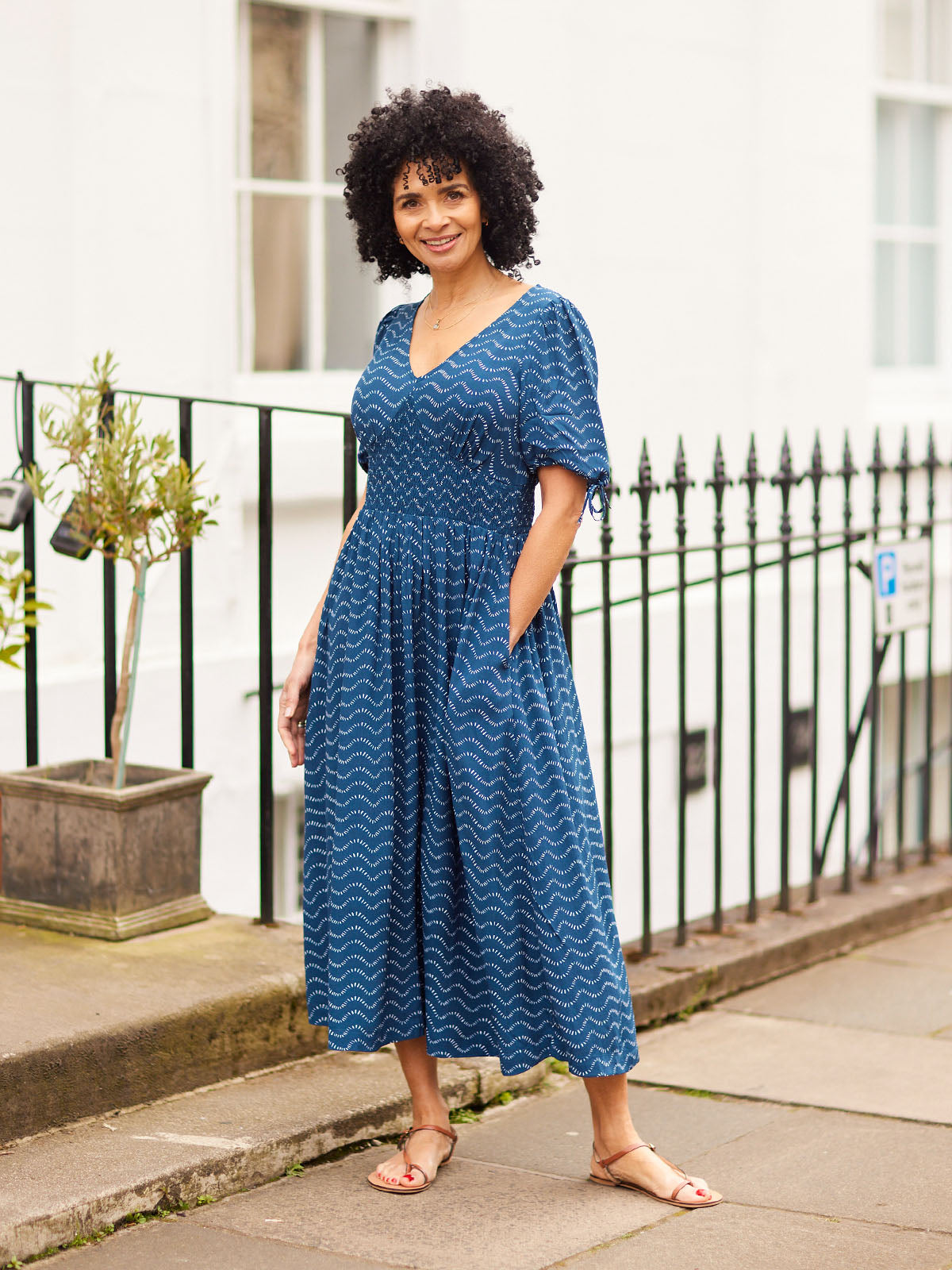 Potted green palm plant on a wooden stand against a light curtain backdrop.