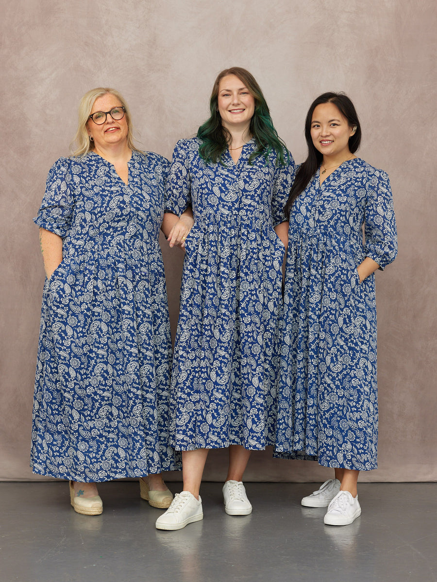 Three models wearing blue and white paisley midi dresses with v-necks, short sleeves, and pockets, styled with white…