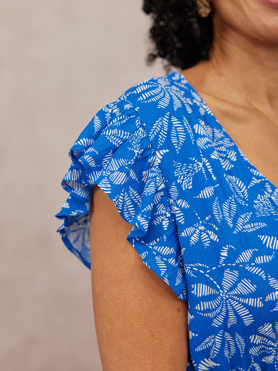 Close-up of a model's shoulder in a blue and white leaf-print dress with a flutter sleeve detail.
