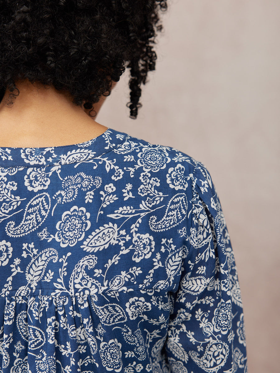 Close-up back view of a model wearing a navy blue top with a white paisley and floral print, featuring a gathered back seam.