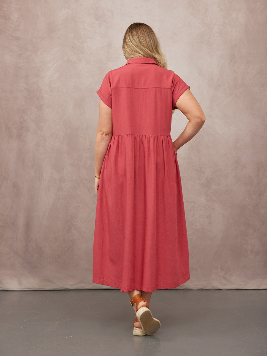 Model seen from behind wearing a coral short-sleeve midi shirtdress with a gathered skirt, paired with tan espadrille wedge…