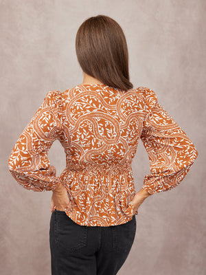 Model seen from behind wearing a rust orange and white floral print blouse with puff sleeves, smocked waist, and dark jeans.