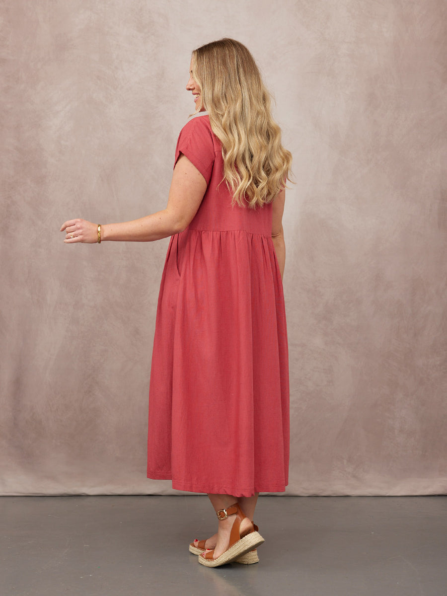 Model seen from behind in a short-sleeve raspberry midi dress with gathered skirt, paired with tan espadrille wedge sandals.