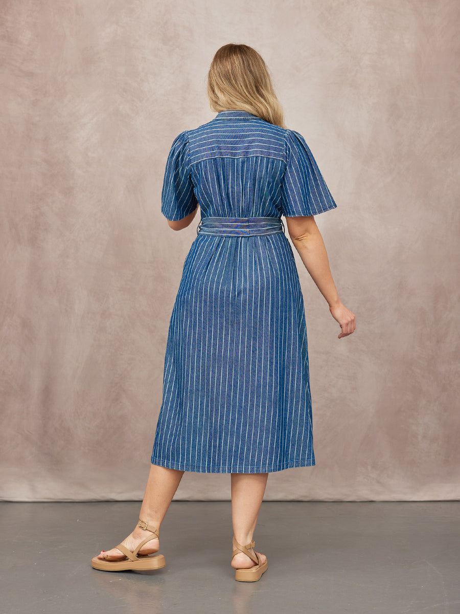 Model seen from behind wearing a blue pinstripe midi dress with puff sleeves and a tie waist, paired with tan platform…