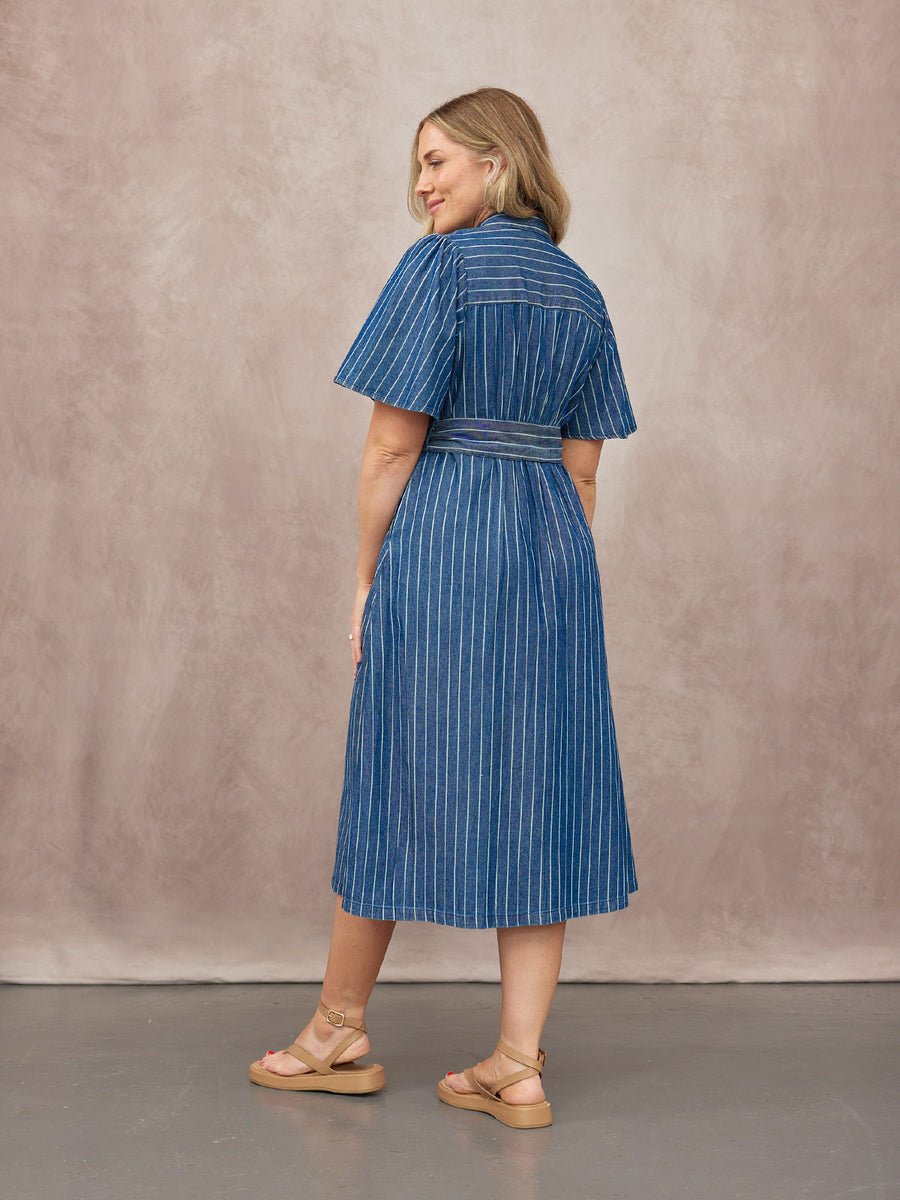 Model wears a blue pinstripe denim midi shirt dress with short flutter sleeves and a tie waist, paired with tan flatform…