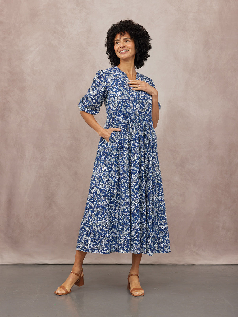 Model wearing a blue and white paisley midi dress with puff sleeves, V-neckline, and tan block-heel sandals.