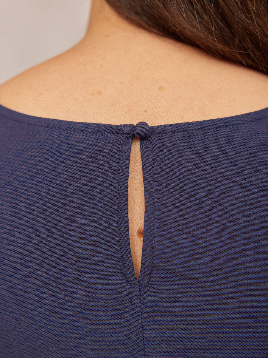 Close-up of a navy blue top's back neckline, showing a teardrop keyhole opening fastened with a fabric-covered button.