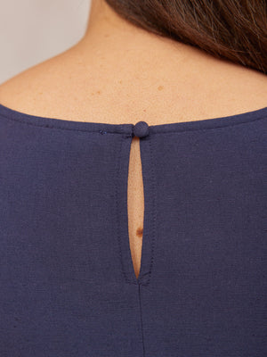 Close-up of a navy blue top's back neckline, showing a teardrop keyhole opening fastened with a fabric-covered button.