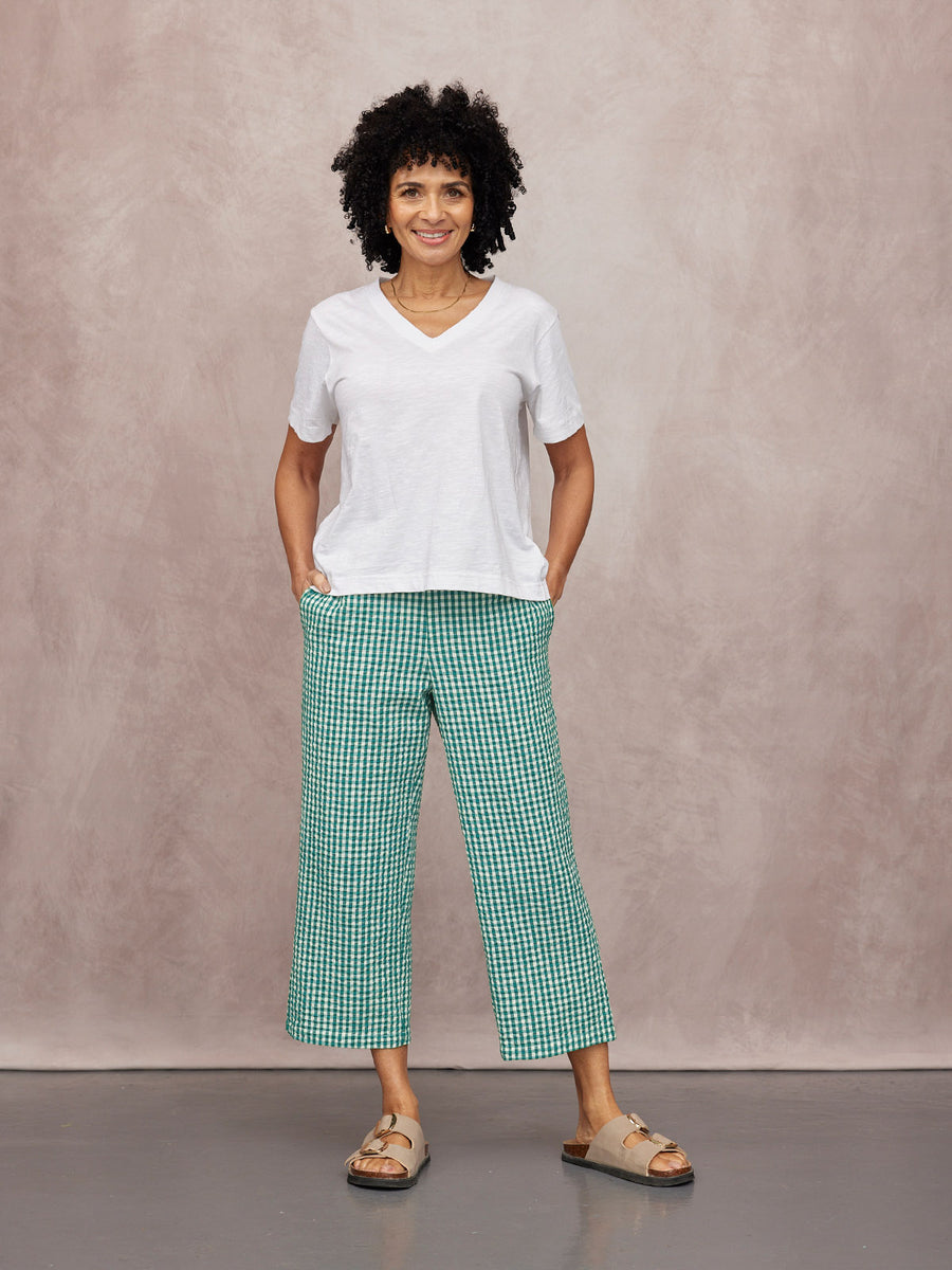 Rhianna Culotte in green gingham, wide-leg cropped trousers worn with white V-neck tee and tan sandals on a studio backdrop.