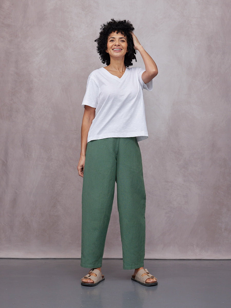 Myrtle Barrel Leg Trouser in green, worn by a woman with white v-neck tee and beige sandals against a studio background