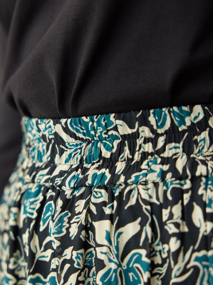 Close-up of a black, teal, and cream floral print skirt with a smocked elasticated waist, paired with a black top.