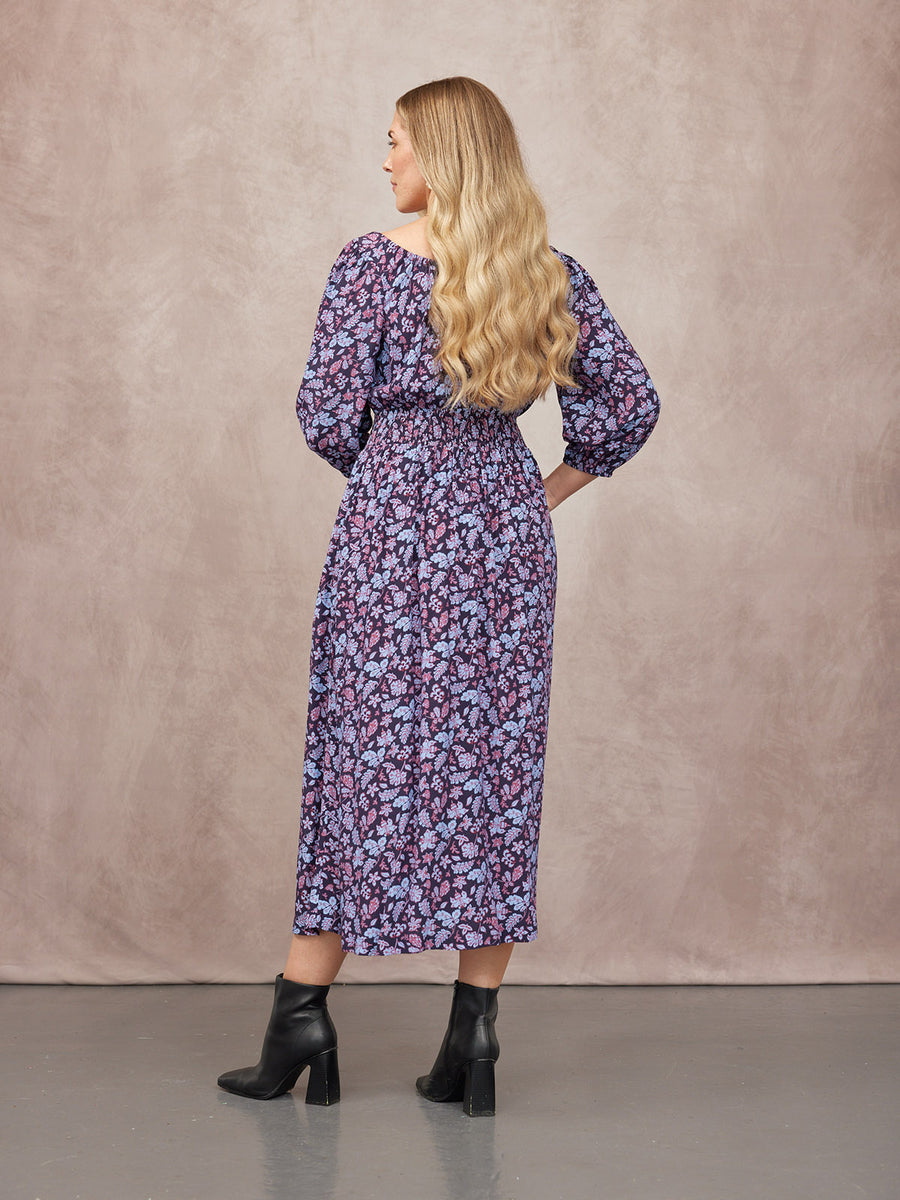 Model seen from behind wearing a navy floral midi dress with puff sleeves and elasticated waist