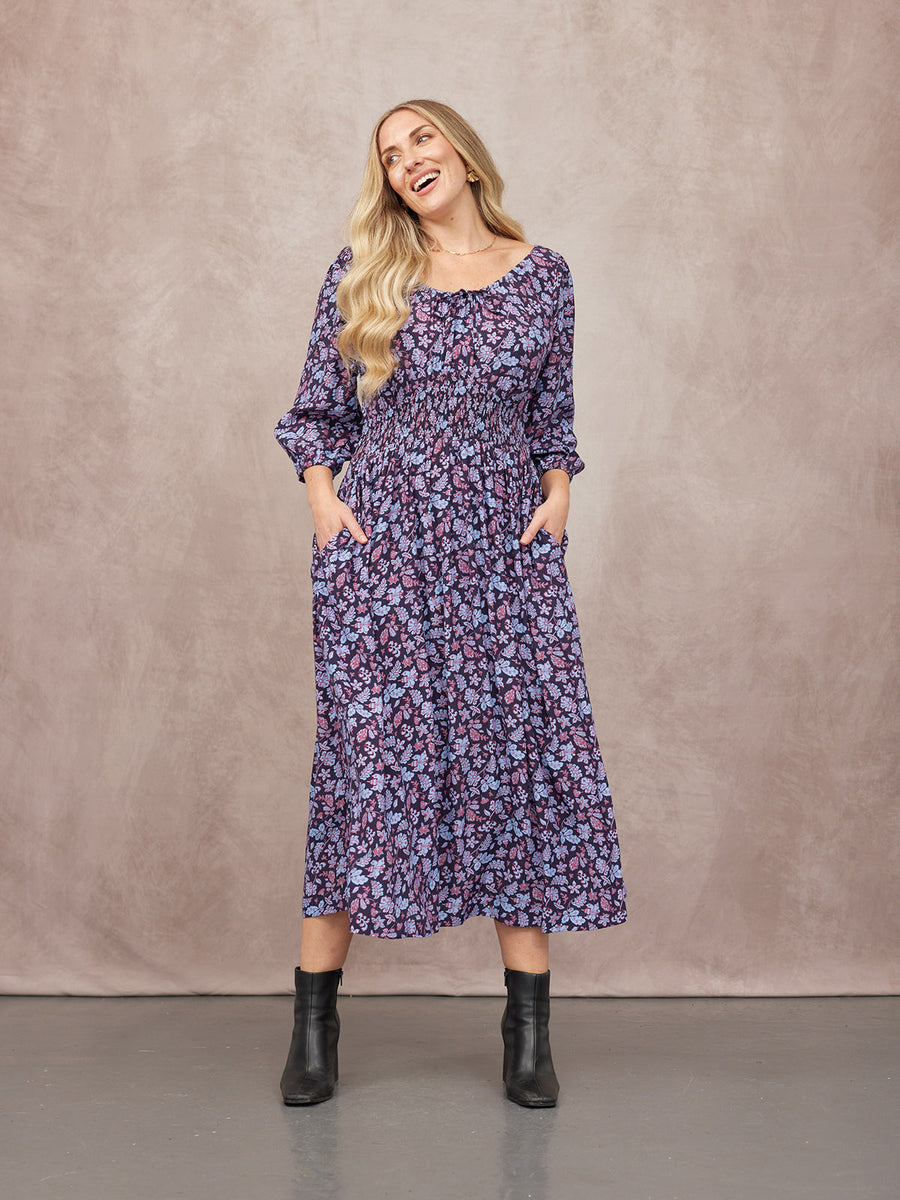 Model wearing a navy floral midi dress with shirred waist, puff sleeves, and pockets, styled with black ankle boots.