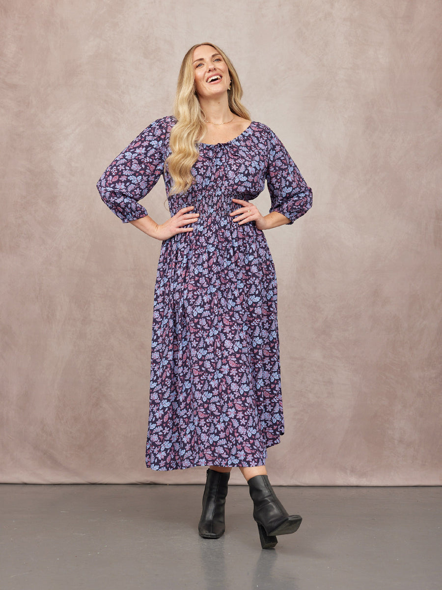 Model wearing a navy floral midi dress with puff sleeves and smocked waist, styled with black ankle boots.