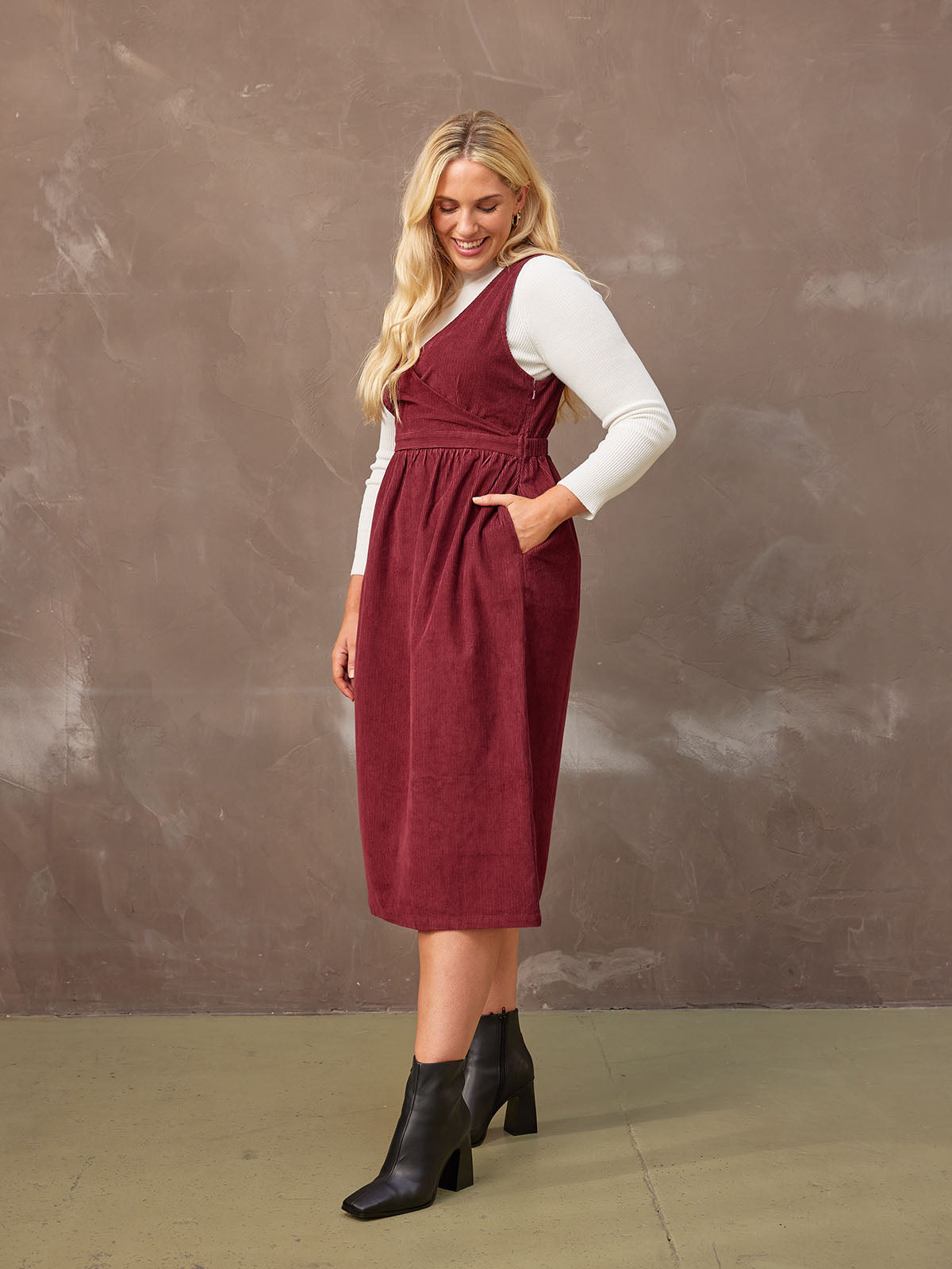 A model poses in the Ally corduroy midi crossover front dress, standing to the side and featuring the pocket detail of the dress.