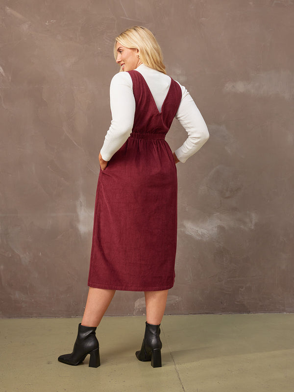 A model poses with her back to the camera, showing the back of the Ally corduroy midi crossover front dress, and the V detail on the back of the dress.
