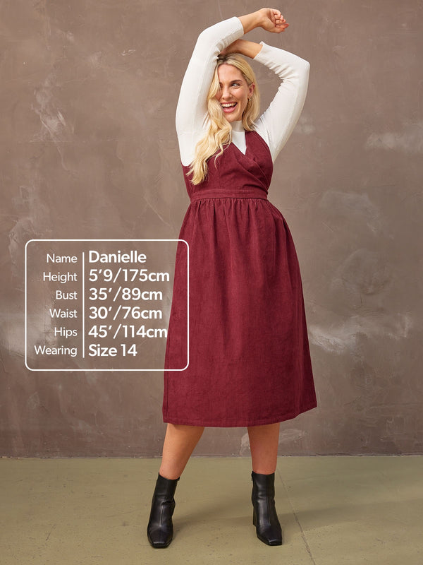 A model wears the burgundy Ally dress styled with a white long-sleeve t-shirt and black boots, with size information annotated on the photo.