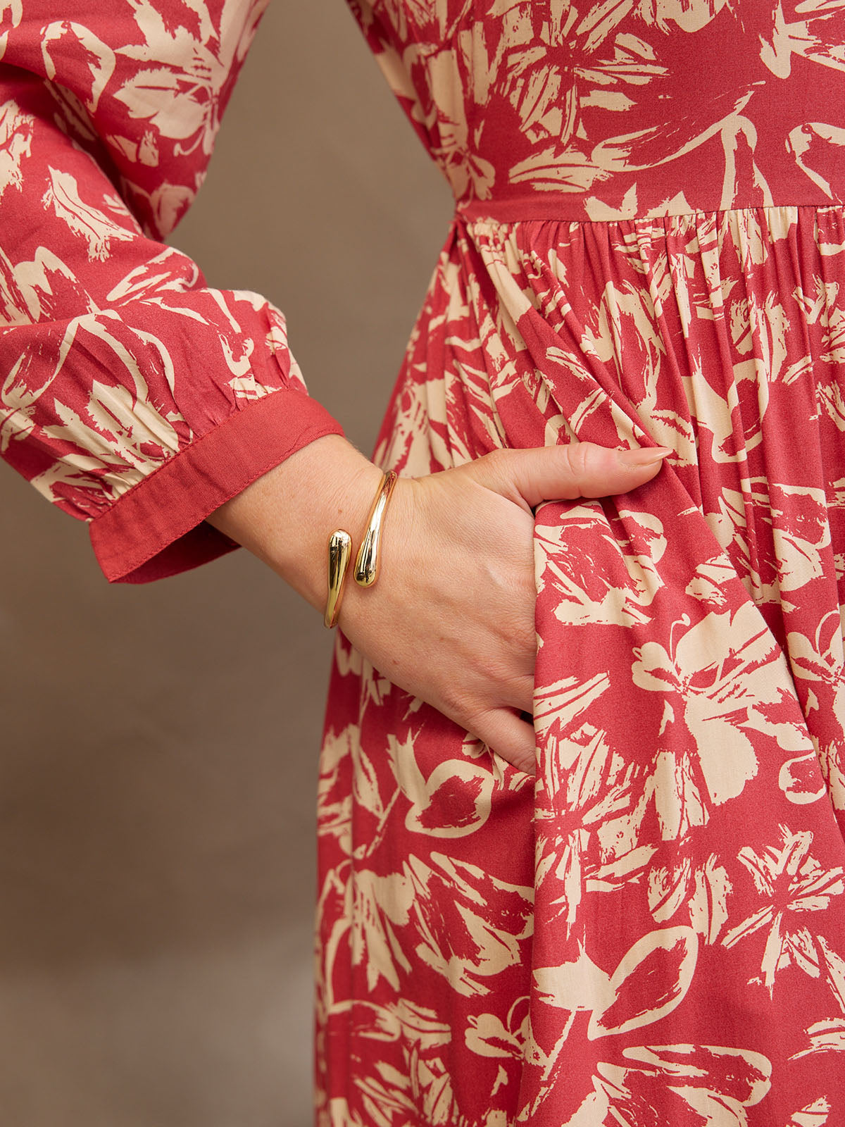 Close-up of a person in a red and white floral dress with a gold bracelet, hand in pocket.