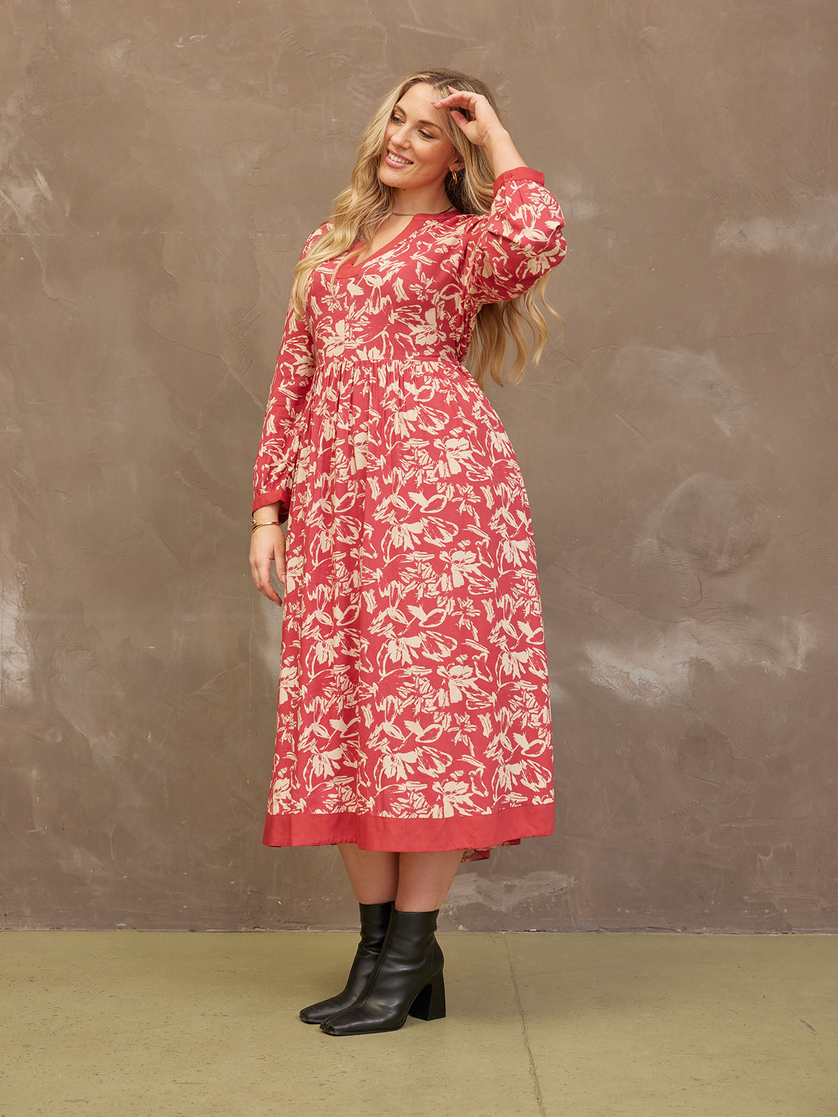 Woman in a floral red dress posing against a textured brown wall.