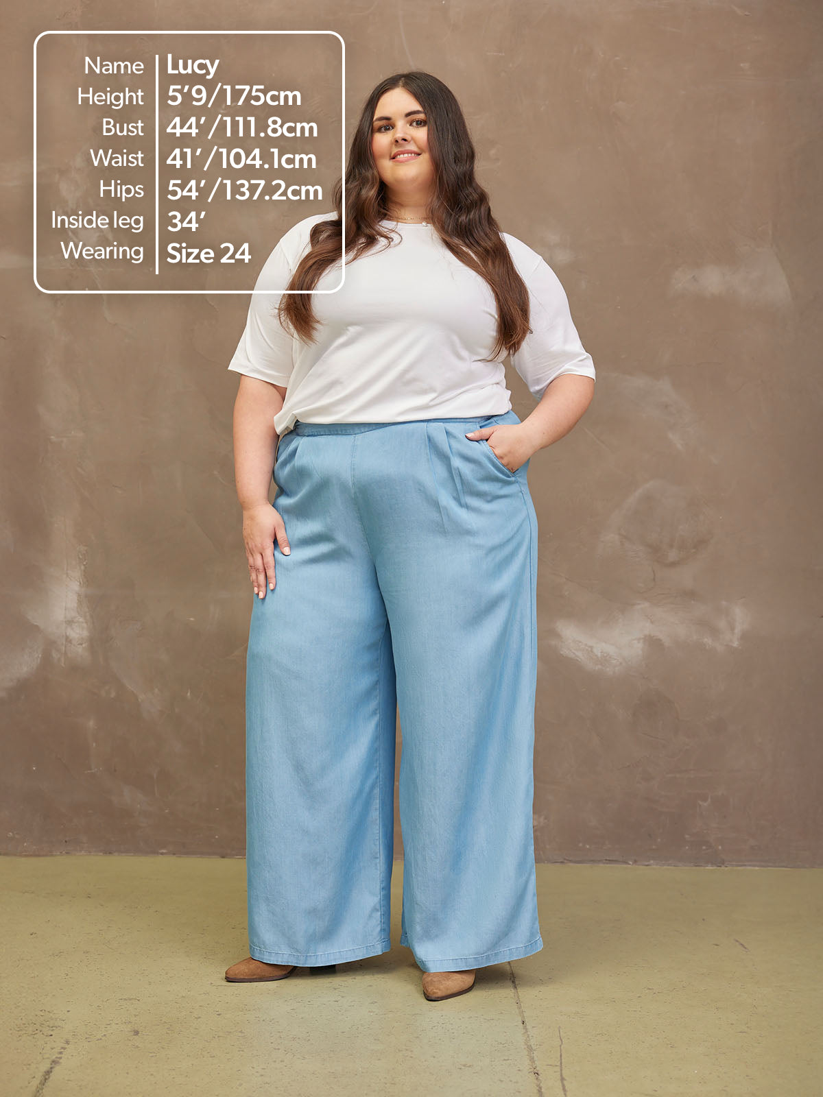 Person posing in a white shirt and blue wide-leg pants against a plain background.