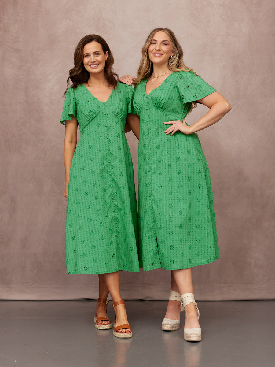 Allegra Broderie Dress in green, V-neck midi with flutter sleeves and button front, worn by two models with wedge sandals