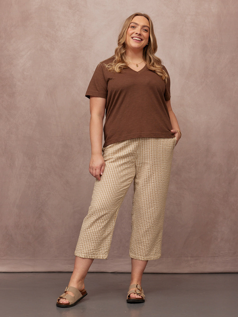 Cathy V-neck Tee in brown, worn by a smiling plus-size model with cropped patterned trousers and tan sandals