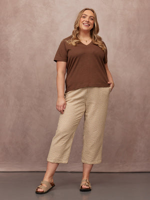 Cathy V-neck Tee in brown, worn by a smiling plus-size model with cropped patterned trousers and tan sandals