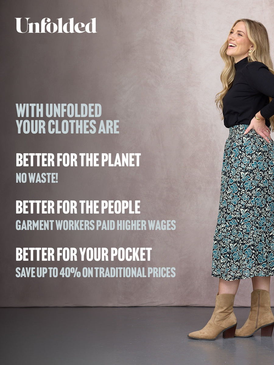 Model wearing a black mock-neck top and teal floral midi skirt with tan ankle boots, smiling against a neutral backdrop.