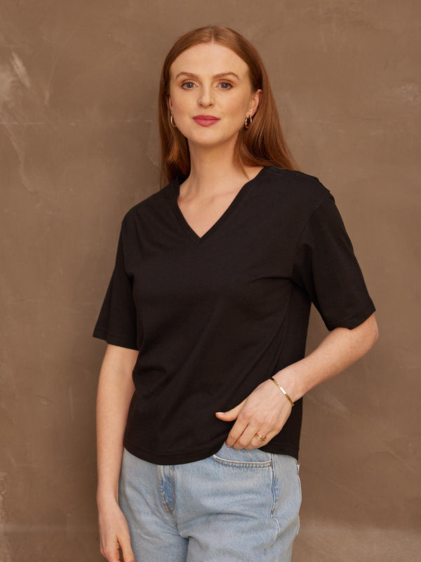 A model looking at the camera with her left hand in her pocket, wearing the sustainable Freya black t-shirt paired with jeans.