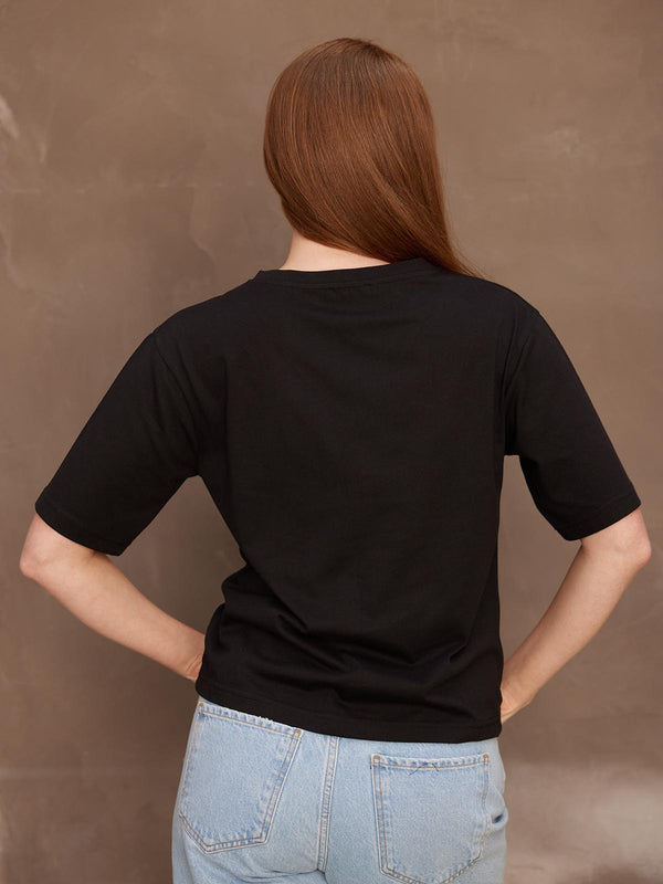 Backview of a model with her hands on her hips, wearing the sustainable Freya black t-shirt paired with jeans.