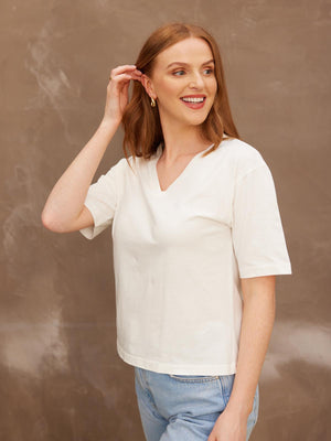 A smiling model looking to the side with her right hand held up to her hair, wearing the sustainable Freya white t-shirt paired with jeans.