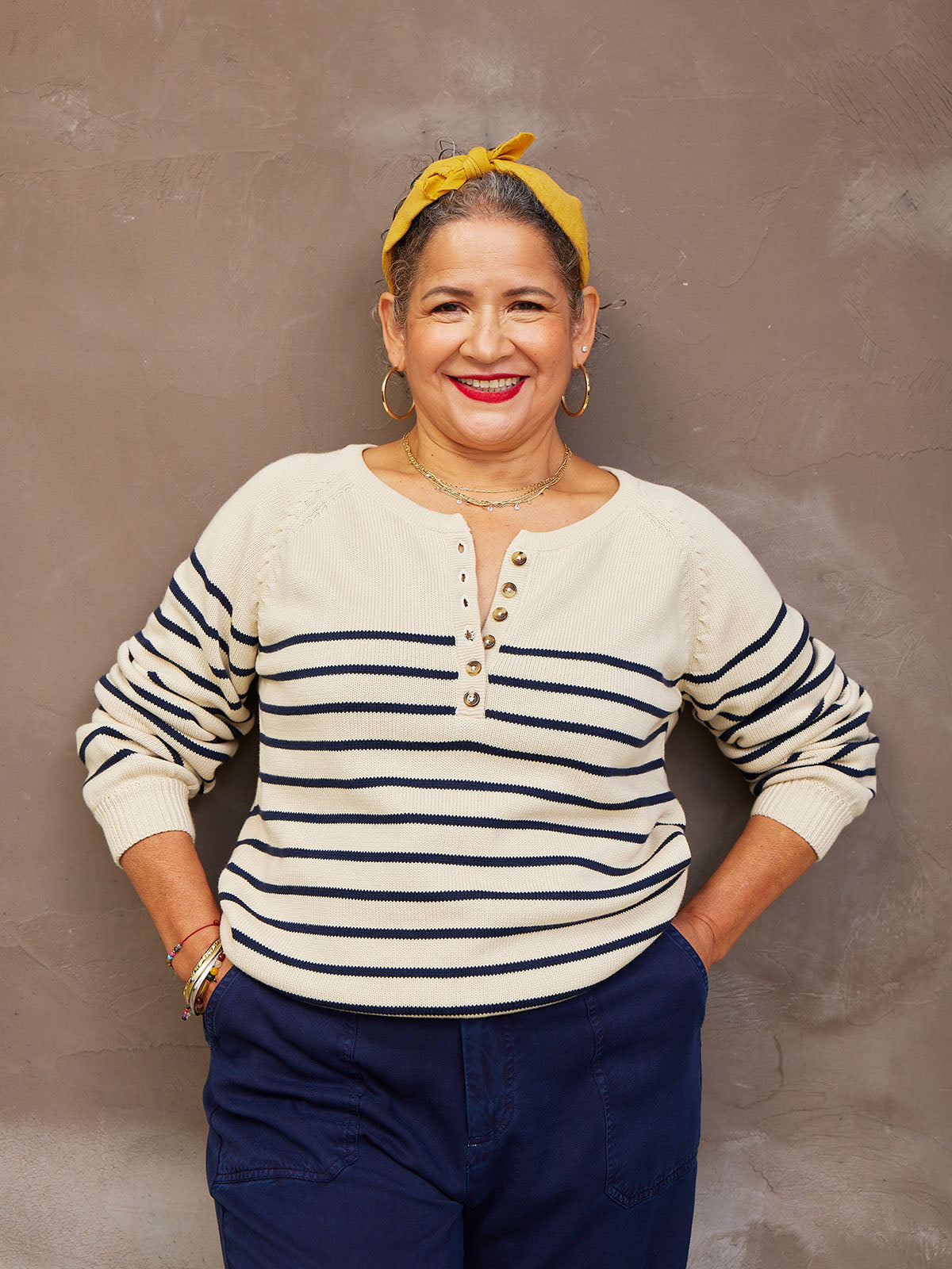 Smiling person wearing a striped sweater and yellow headband against a plain background.