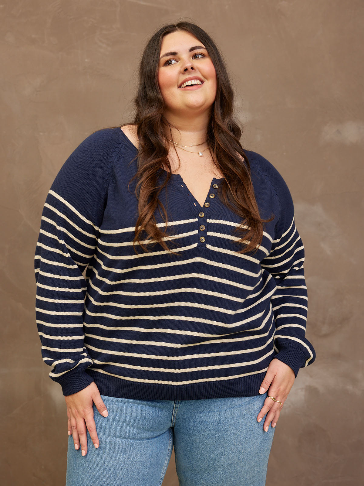 Person wearing a striped navy sweater and blue jeans against a neutral background.