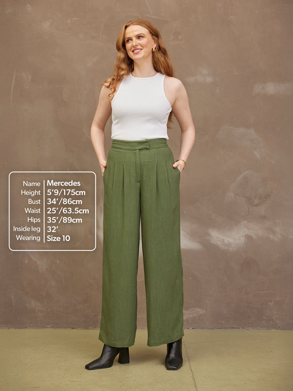 Woman wearing a white top and green pants, standing against a neutral background.