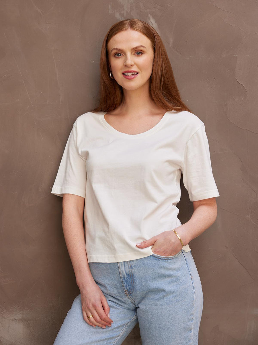 A smiling model with her left hand in her pocket, wearing the sustainable Lucy white t-shirt paired with jeans.