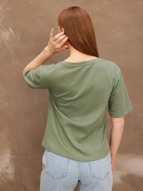 Backview of a model with her left hand held up to her ear, wearing the sustainable Lucy khaki t-shirt paired with jeans.