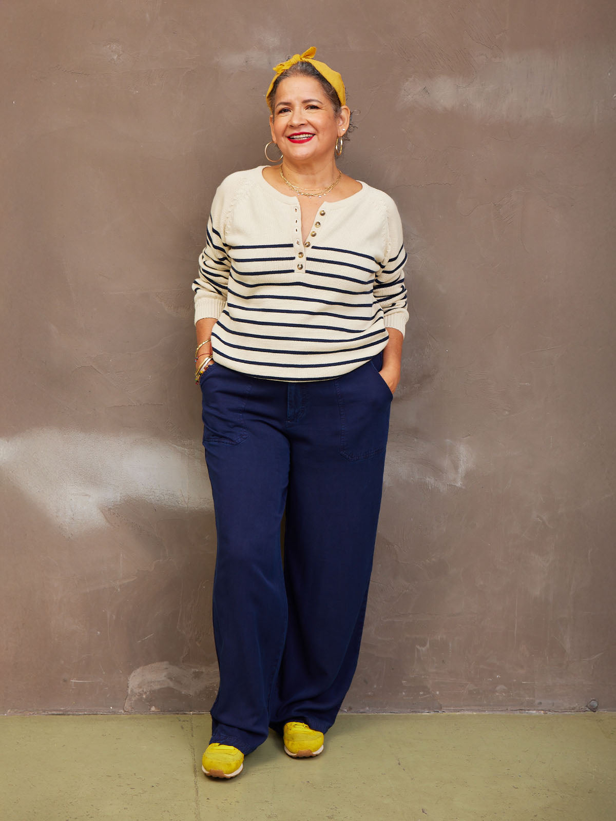 A person wearing a striped sweater, blue pants, and yellow shoes, standing against a plain background.