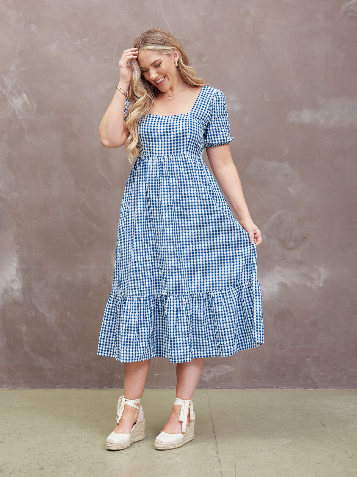 Woman in a blue checkered dress smiling against a neutral background.