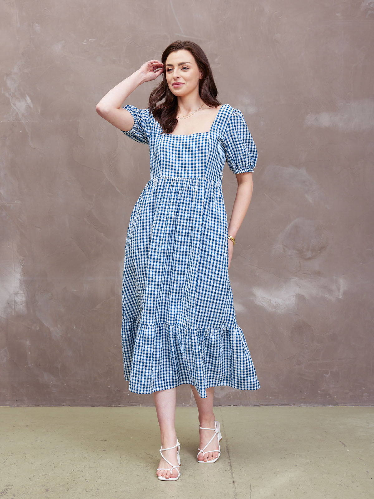 Woman in a blue checkered dress against a neutral background.