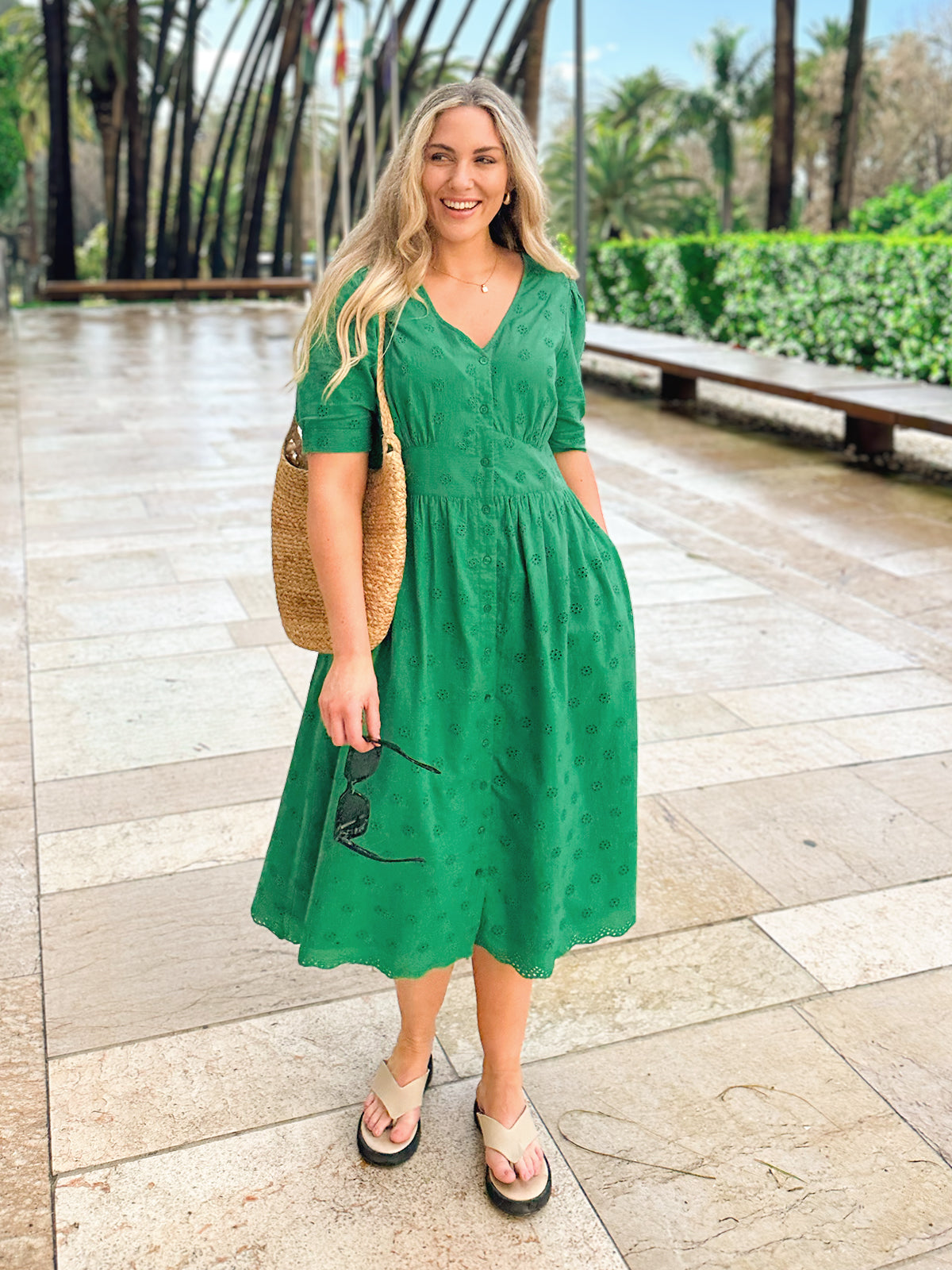 Woman in green dress standing on a stone pathway with palm trees.