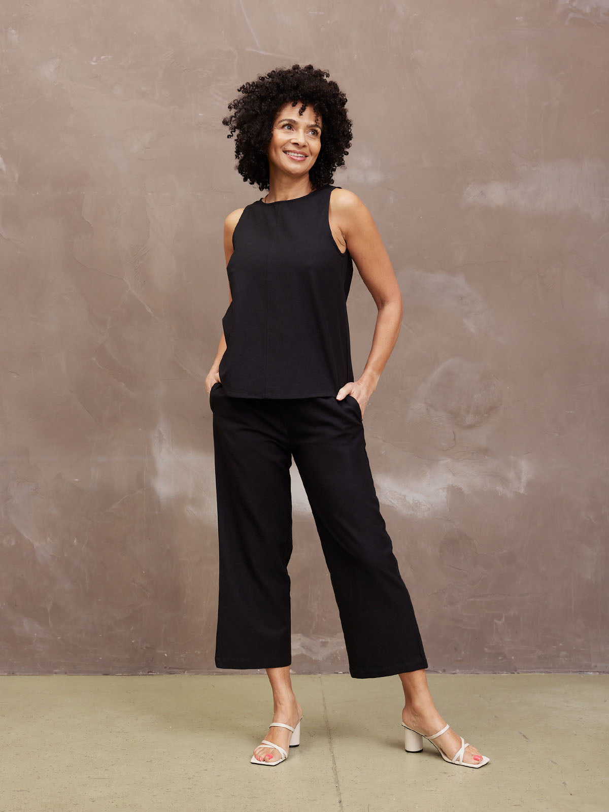 A woman in black outfit stands against a textured wall.