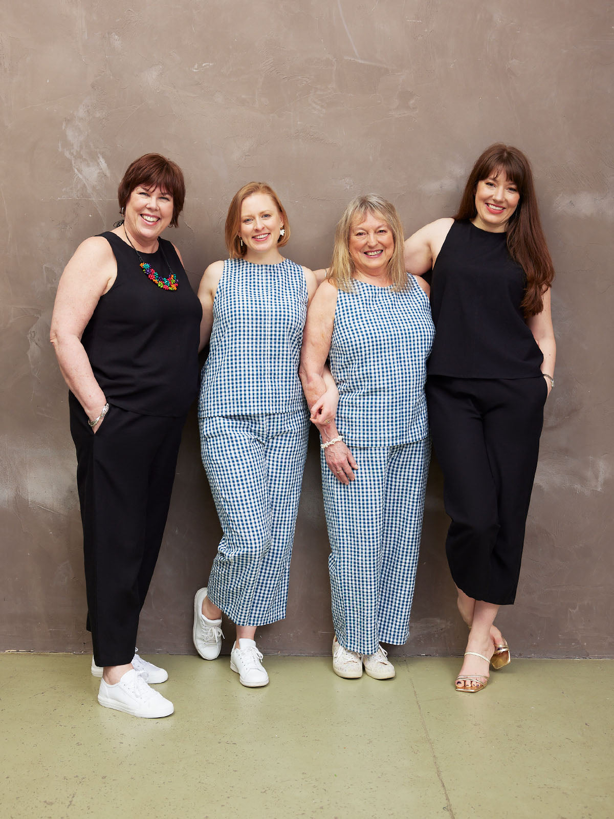 Four women standing together, smiling, wearing casual coordinated outfits.