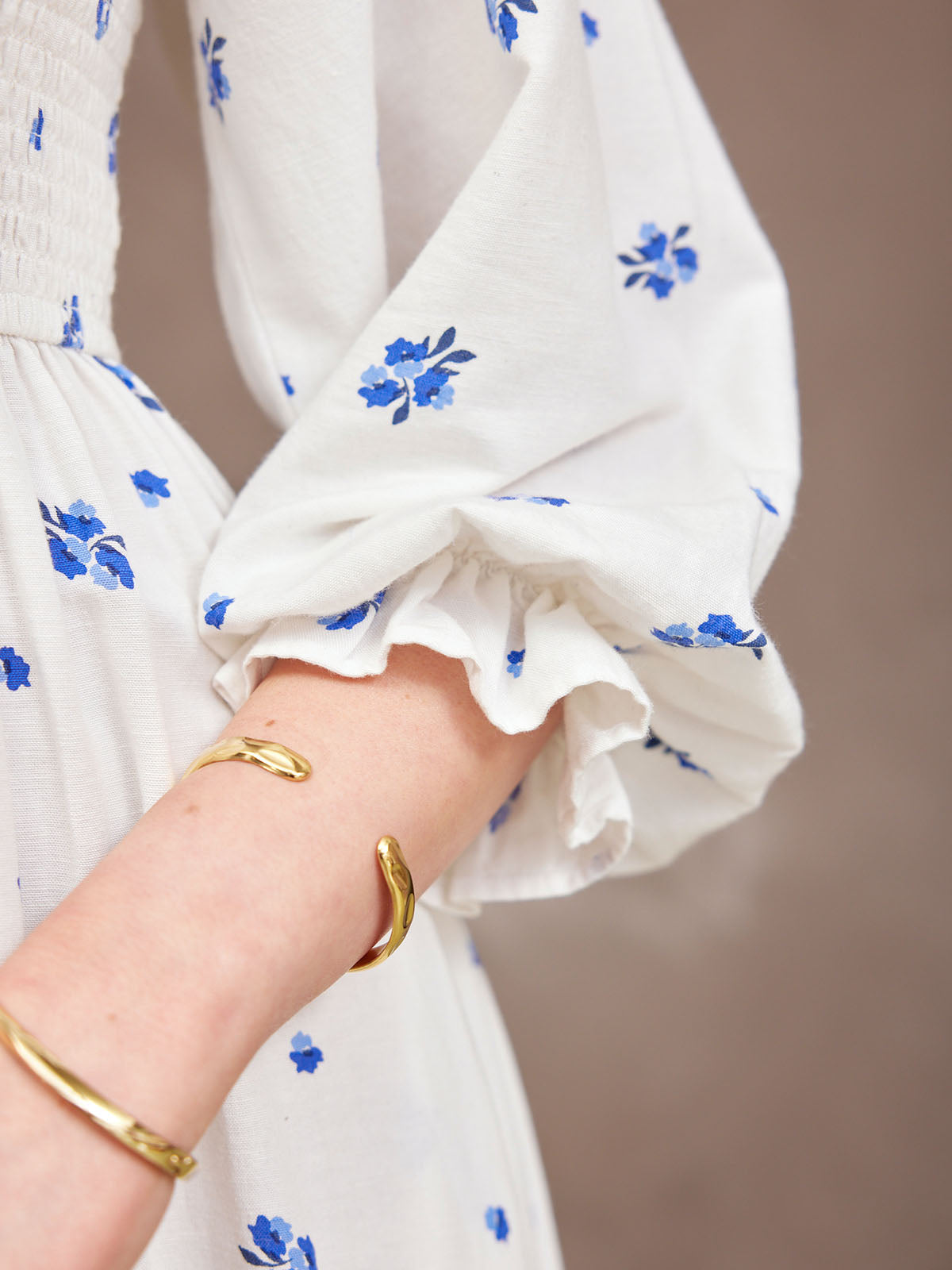 Close-up of a white dress with blue floral patterns and gold bracelets on a wrist.
