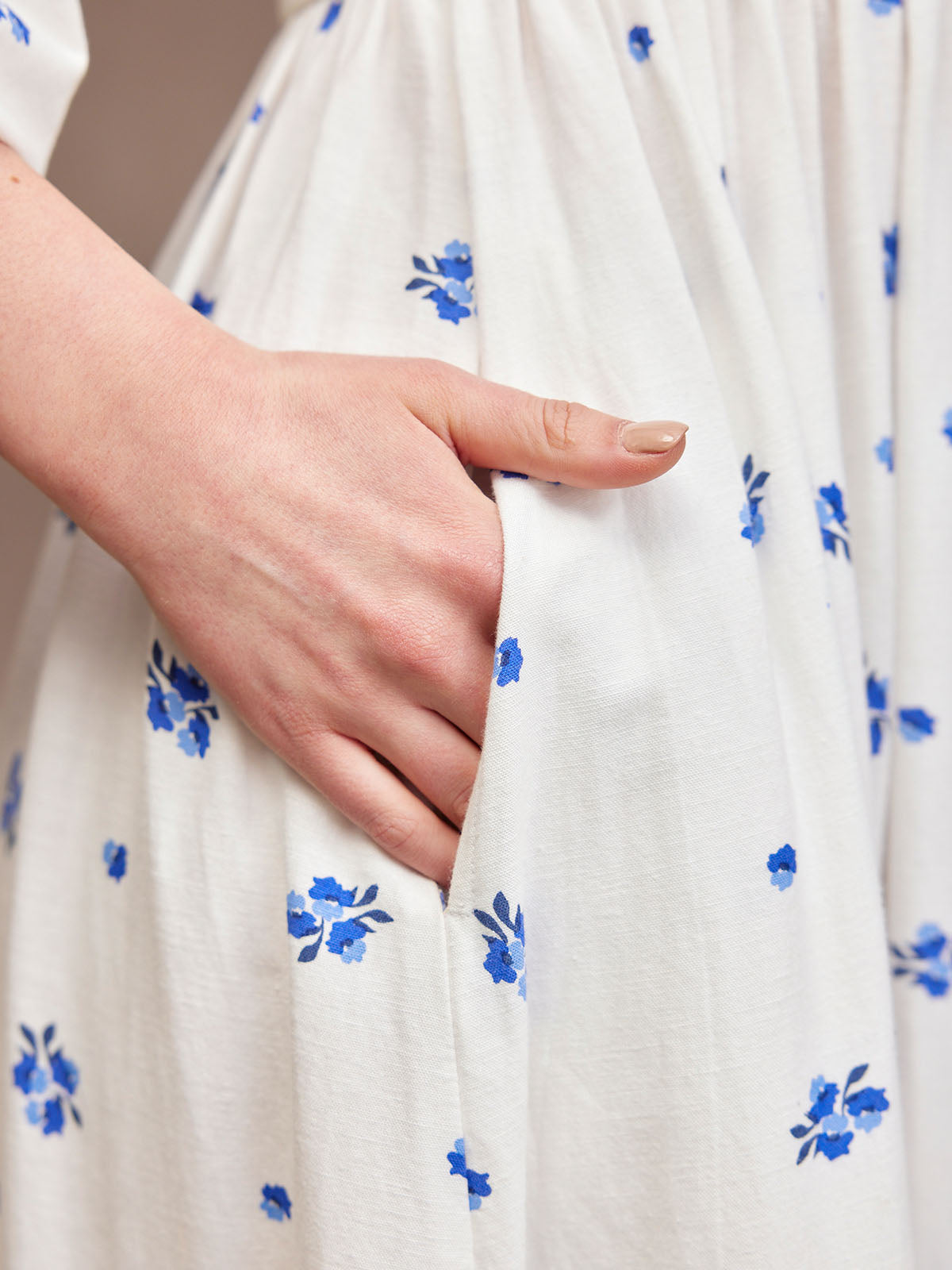 Hand in pocket of white dress with blue floral pattern.