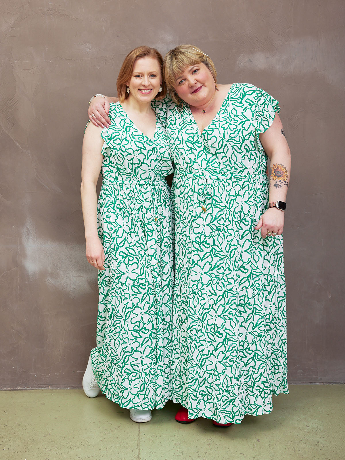 Two people in matching floral dresses pose happily against a textured background.