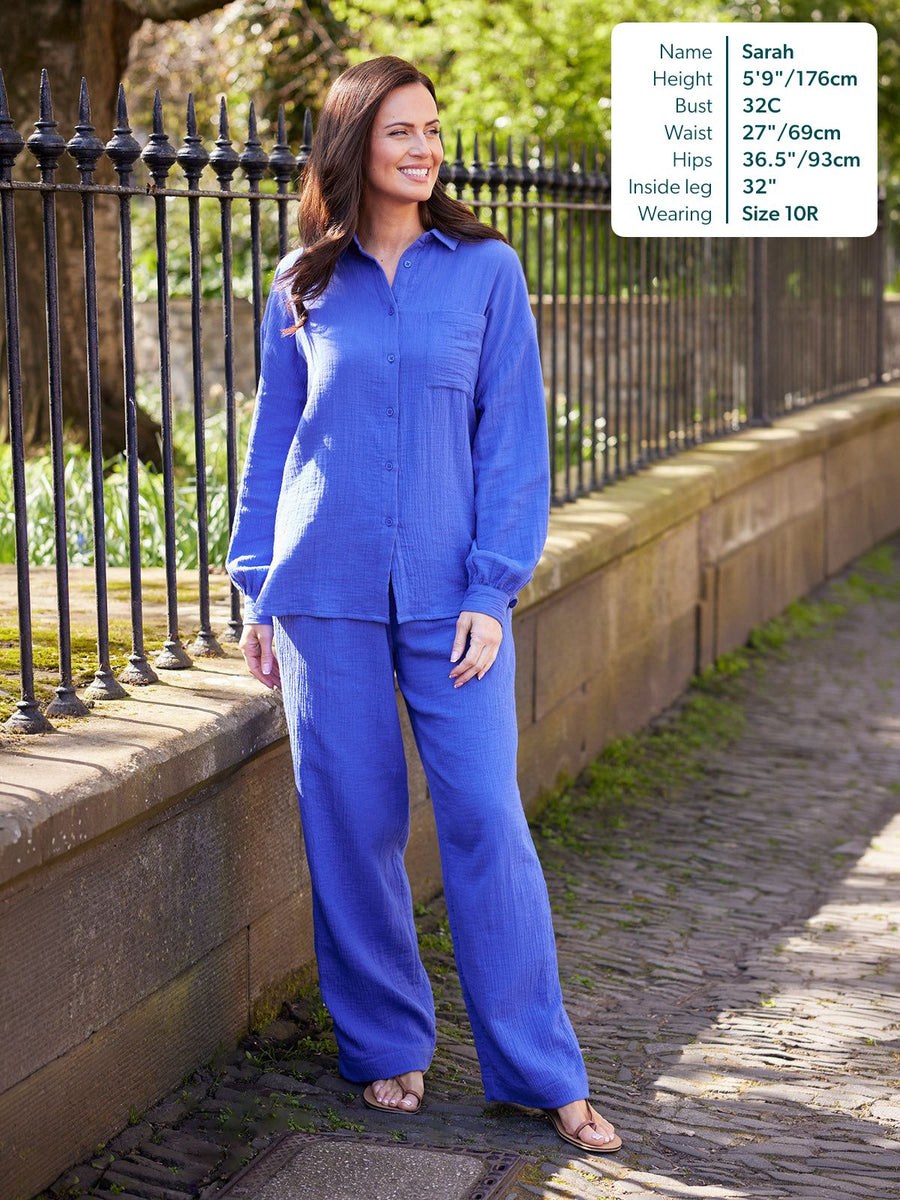 Joy Cotton Crinkle Trouser in cobalt blue, wide-leg fit, worn with matching shirt and sandals on a cobblestone path.