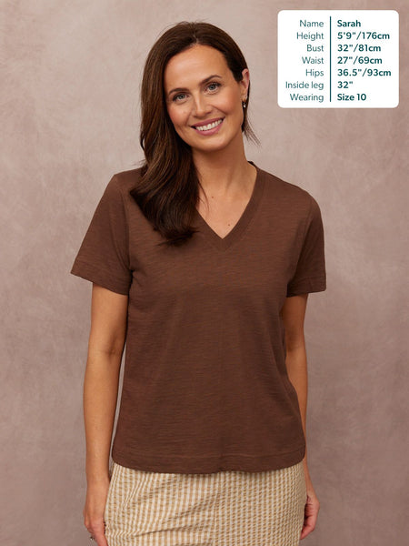 Cathy V-neck Tee in brown, worn by a smiling woman paired with a striped skirt, short sleeves, relaxed fit