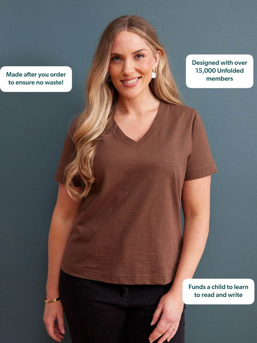 Cathy V-neck Tee in brown, worn by a smiling woman with dark jeans against a grey-blue studio background