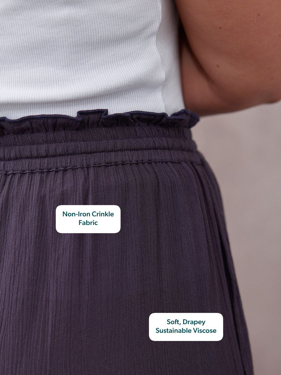 Close-up of a navy crinkle-fabric wide-leg trouser with a frill elasticated waist, styled with a white ribbed top.