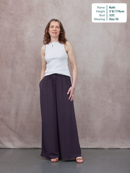 Model wearing wide-leg dark purple trousers with a drawstring waist and a white sleeveless top, styled with tan sandals.